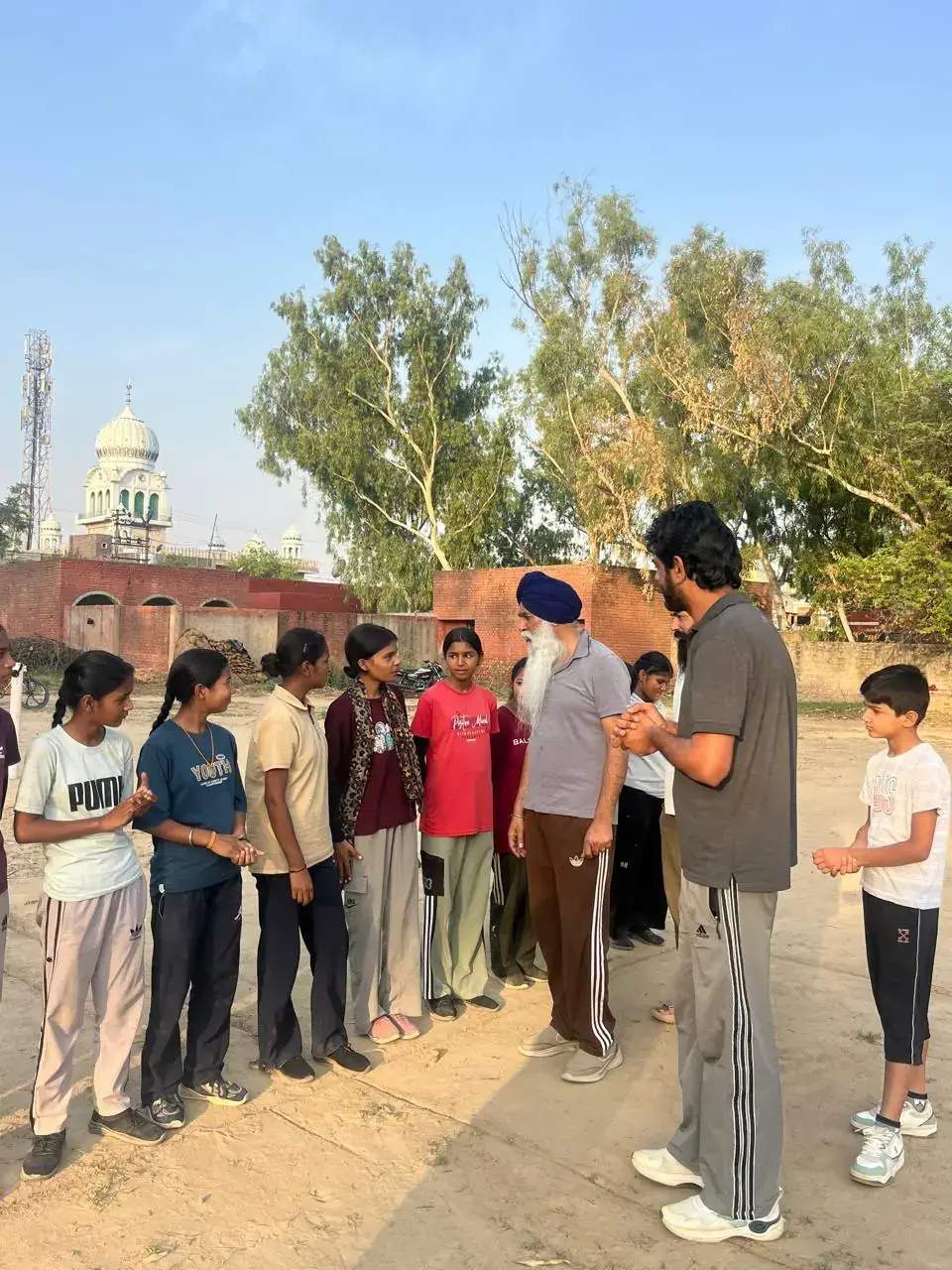 Two men talking with a group of girls on a sports ground in Surtia, Sirsa