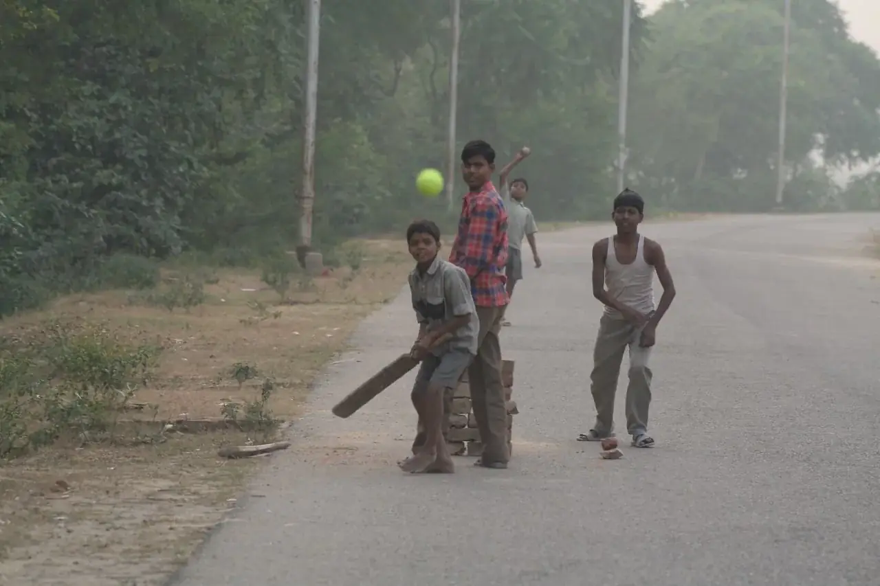 Children playing cricket on a quiet road at dawn