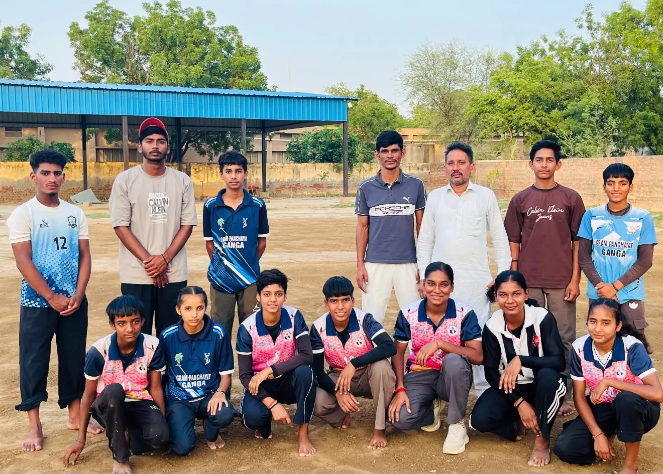 Boys and girls in Gram Panchayat Ganga sports jerseys posing with their coach on a dirt ground