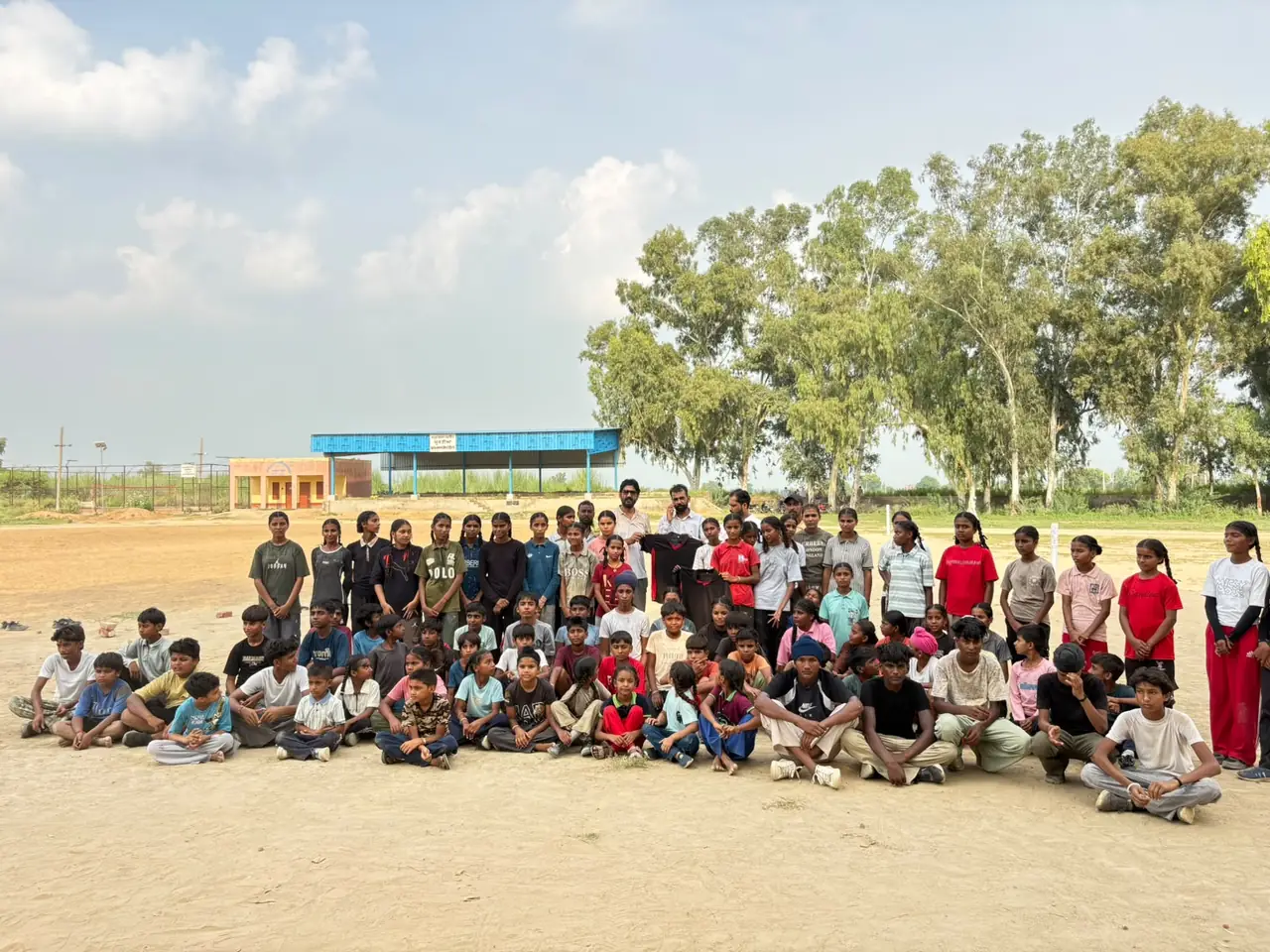 Children seated and standing for a group photograph on the sports ground at Surtia, eucalyptus trees behind