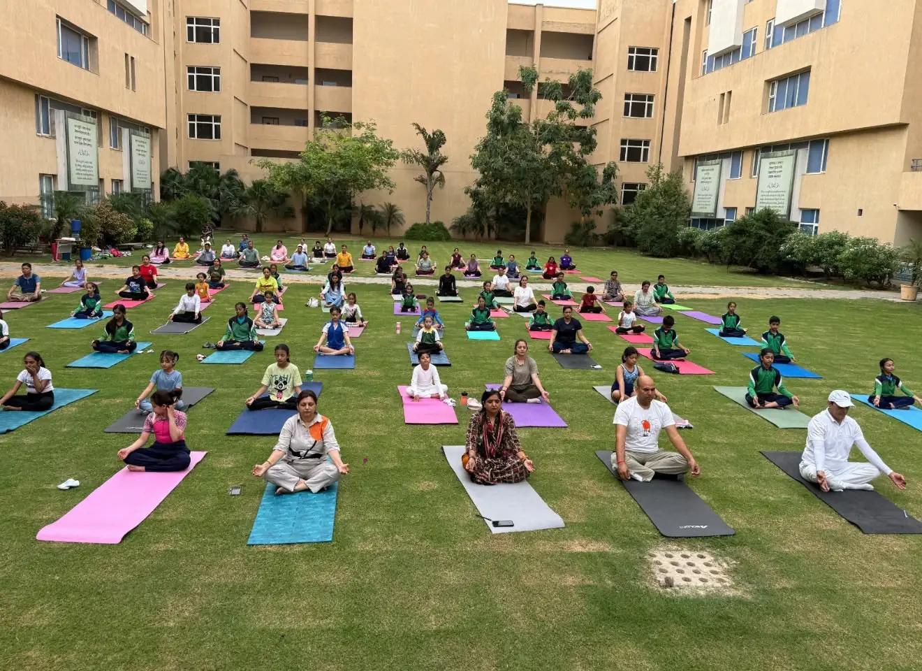 Rows of children and adults seated on yoga mats on a school lawn